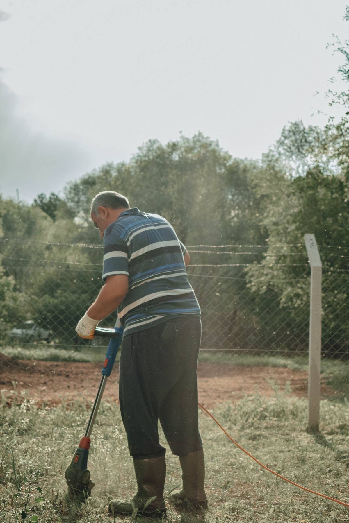 Gardener edging along a fence with a grass trimmer