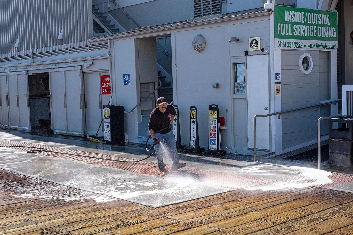Worker pressure washing a paved path beside a building