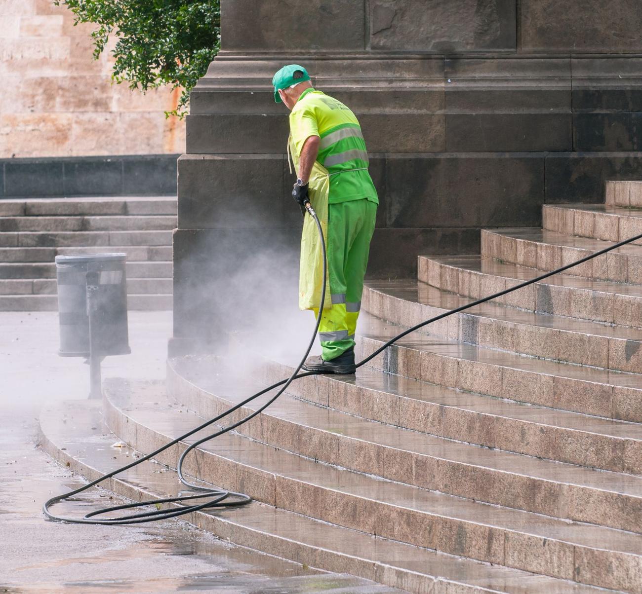 Worker pressure washing stone stairs in a public space